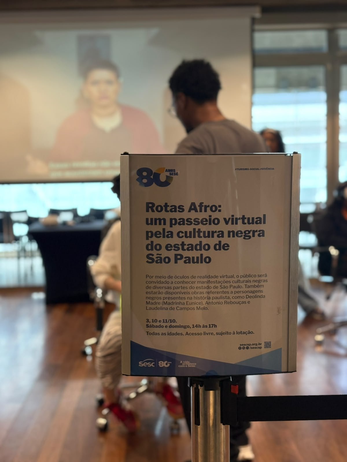 Placa de apresentação do Rotas Afro com a atividade ao fundo